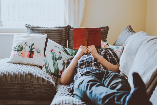 muž s knihou ležící na gauči